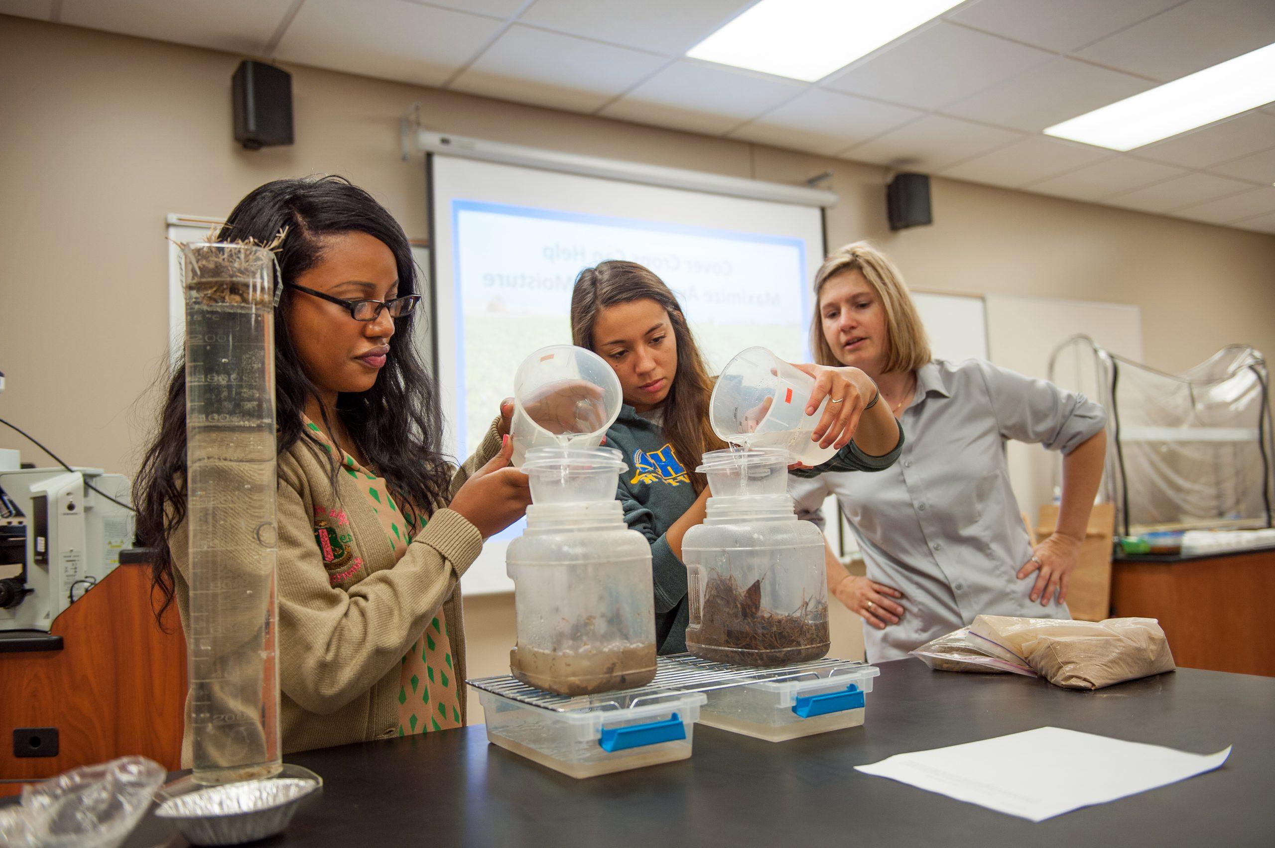 Two students with an instructor conducting a 土壤 and 水 experiment in class.